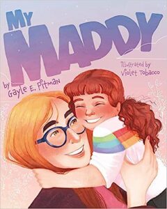 The illustrated cover of My Maddy. A child in a rainbow shirt squeezes their non-binary parent in a tight hug. Their parent has blond hair and big blue glasses. Everyone is smiling.